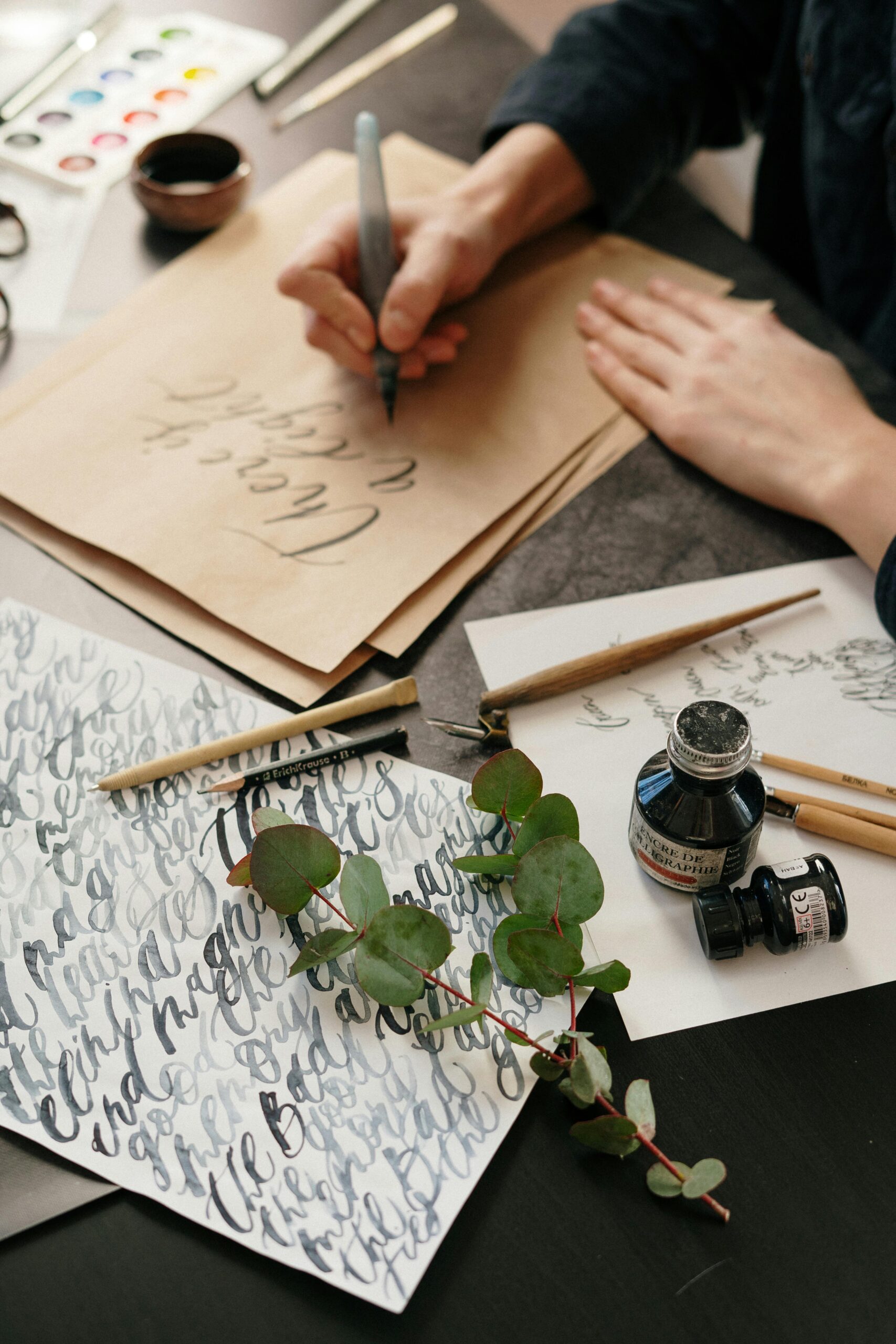 Elegant hand lettering setup with ink, paper, and eucalyptus, showcasing creativity.